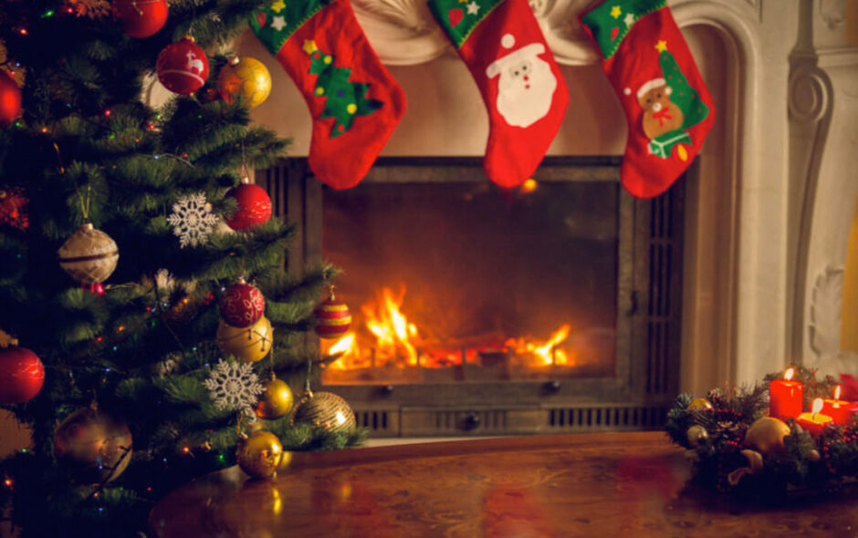 Caminetto natalizio acceso con calze di babbo natale appese e albero di natale con palle decorative acceso